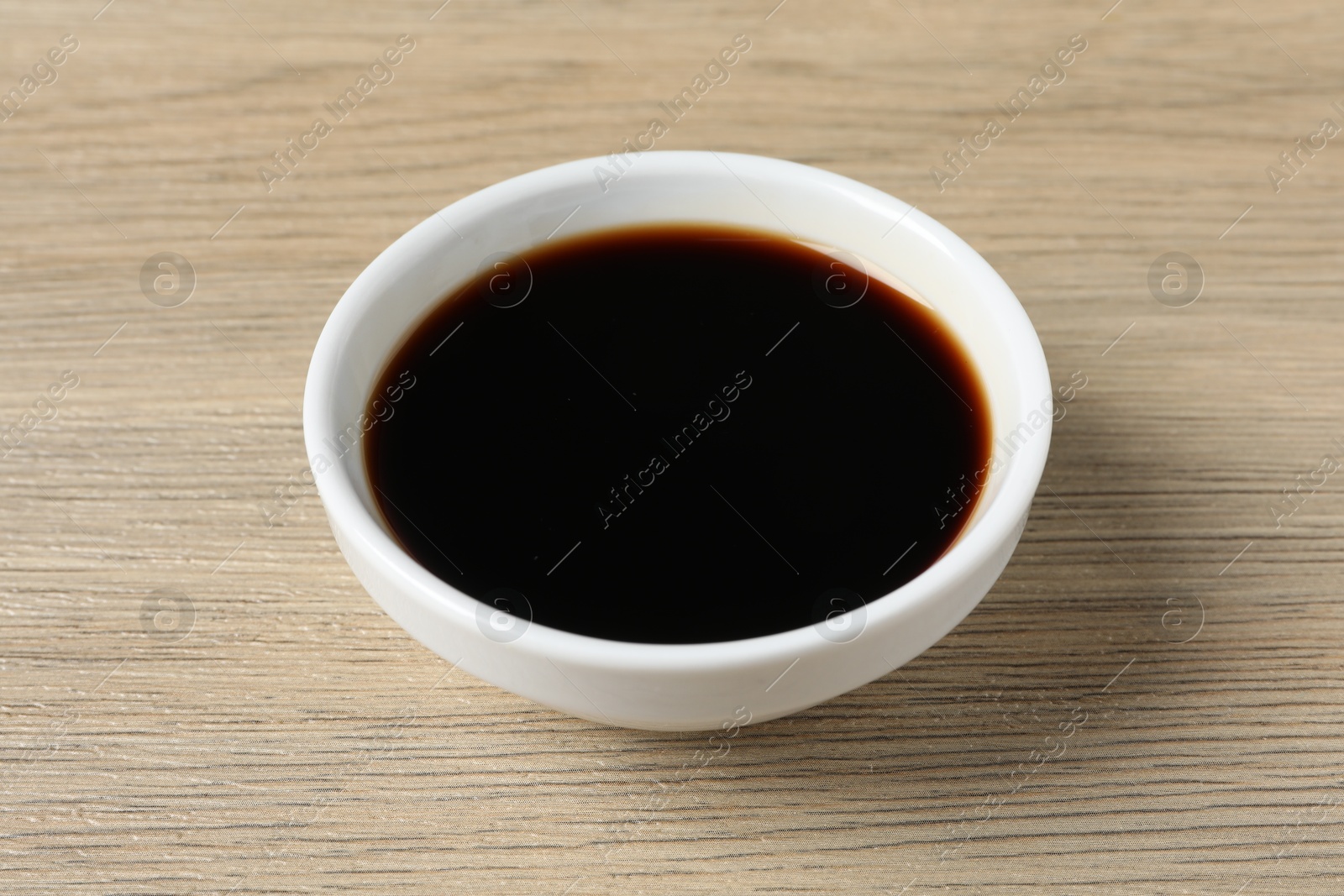 Photo of Balsamic vinegar in bowl on light wooden table