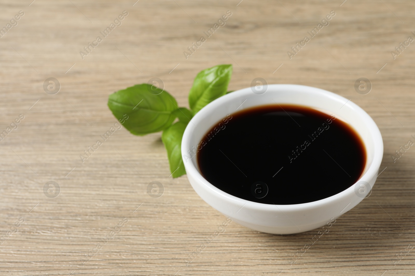 Photo of Balsamic vinegar and basil on light wooden table, space for text