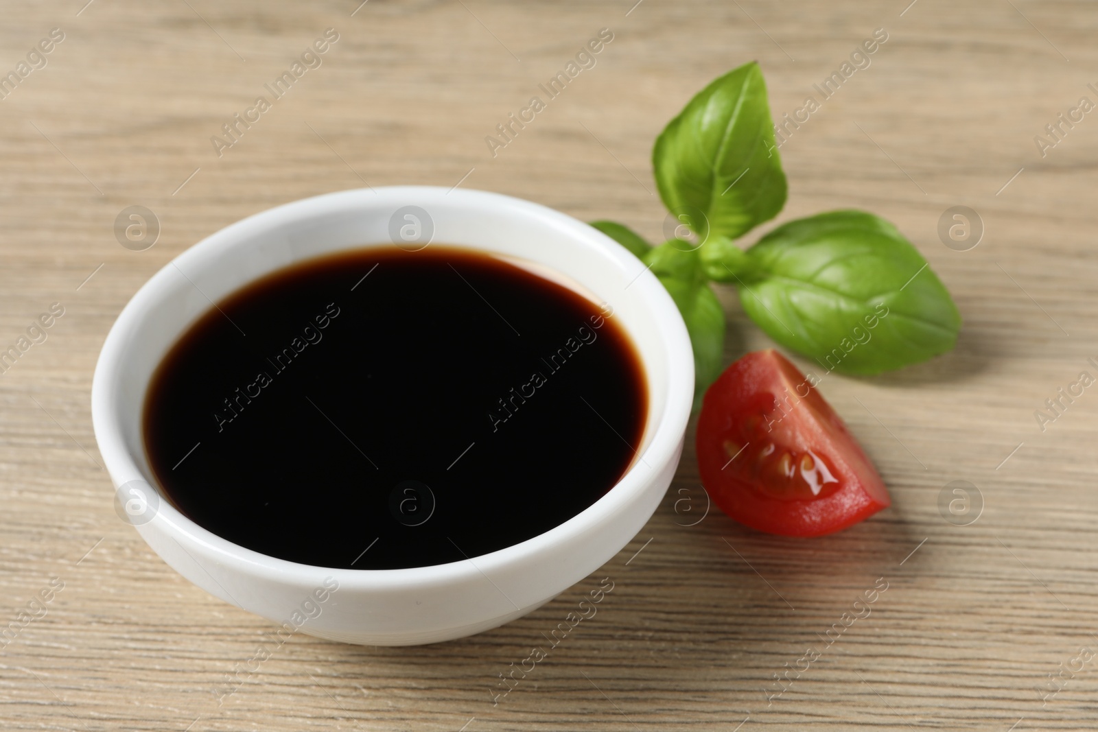 Photo of Balsamic vinegar, tomato and basil on light wooden table