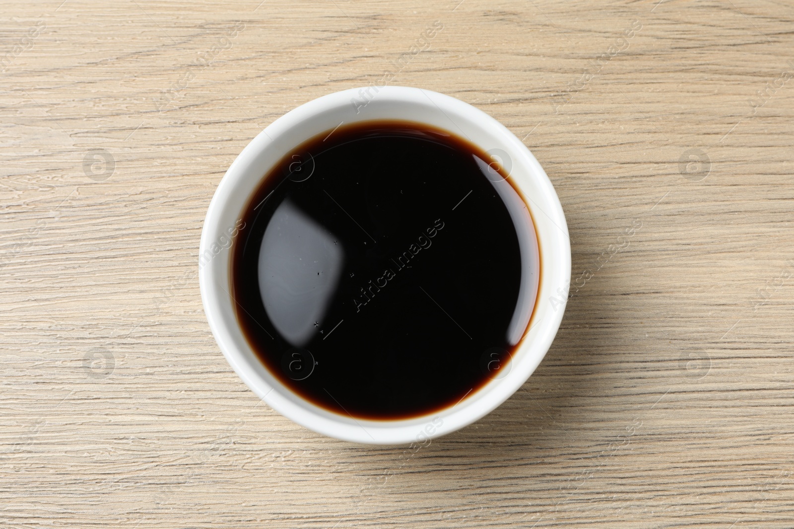 Photo of Balsamic vinegar in bowl on light wooden table, top view