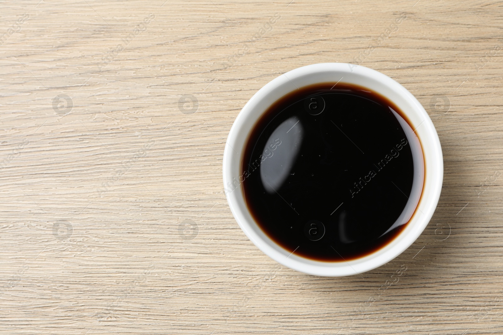 Photo of Balsamic vinegar in bowl on light wooden table, top view. Space for text