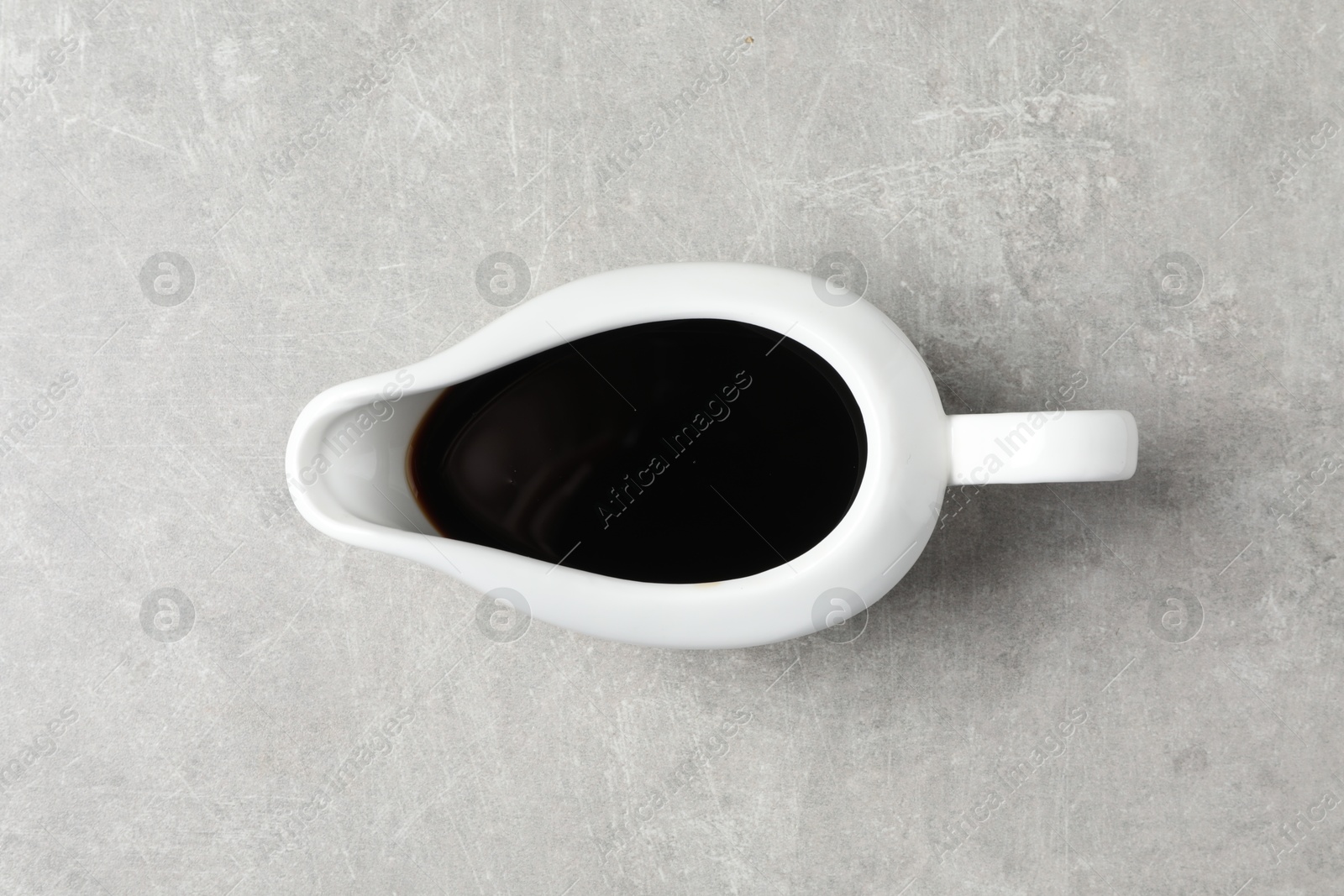 Photo of Balsamic vinegar in sauce boat on light grey table, top view