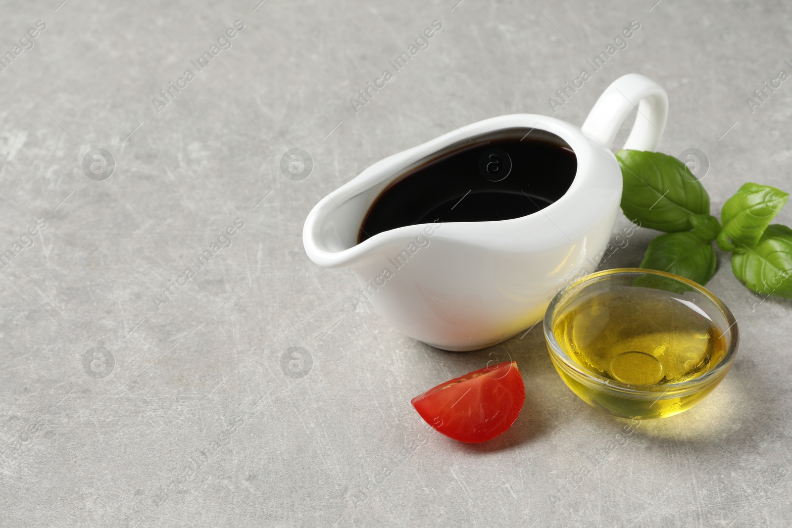 Photo of Balsamic vinegar, oil, tomato and basil on light grey table, space for text