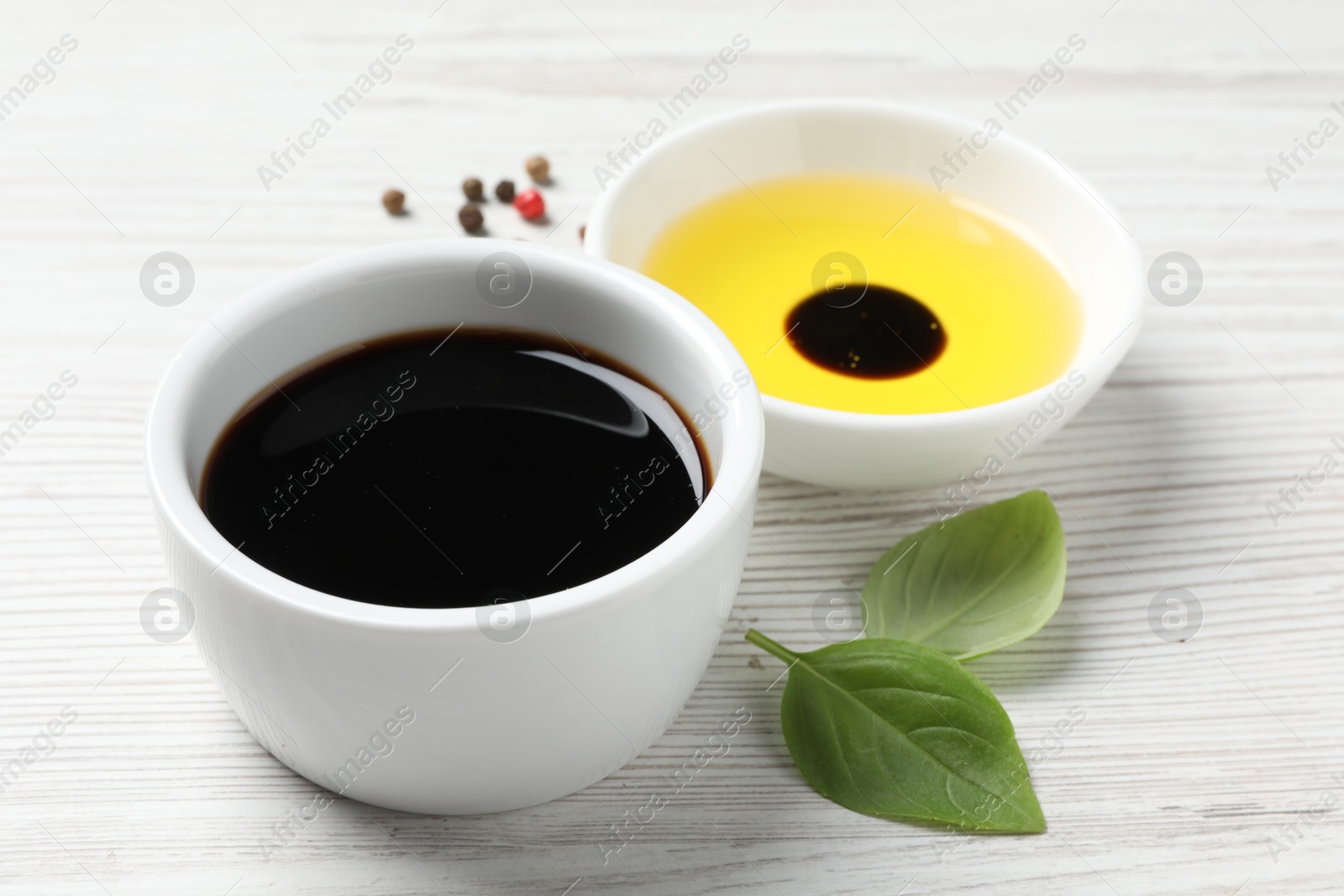 Photo of Balsamic vinegar, oil, peppercorns and basil on white wooden table