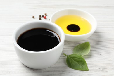 Photo of Balsamic vinegar, oil, peppercorns and basil on white wooden table