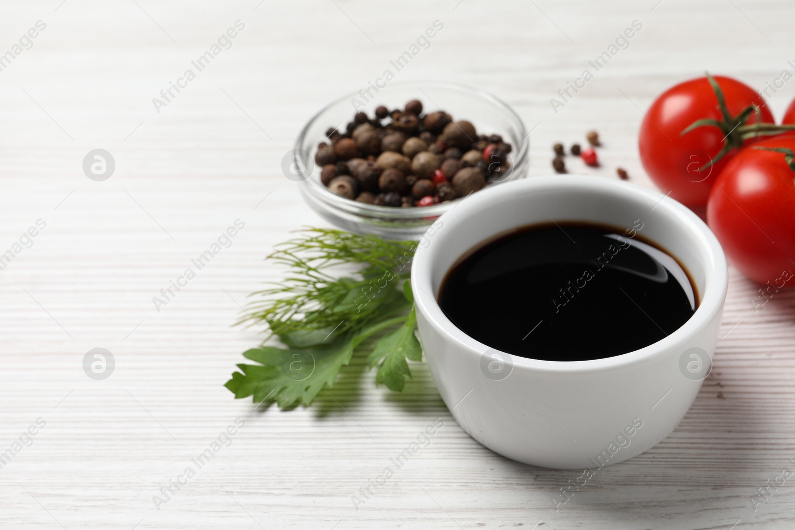 Photo of Balsamic vinegar, tomatoes, peppercorns and herbs on white wooden table, space for text