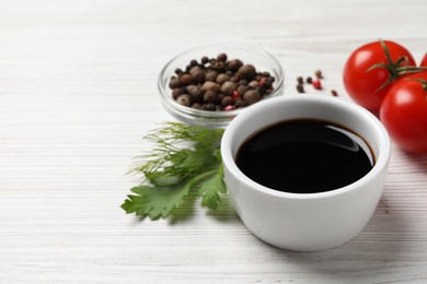 Photo of Balsamic vinegar, tomatoes, peppercorns and herbs on white wooden table, space for text