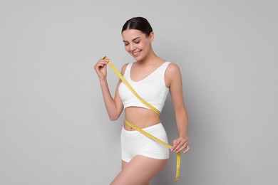 Photo of Diet and weight loss concept. Beautiful young woman with measuring tape showing her slim body against light grey background