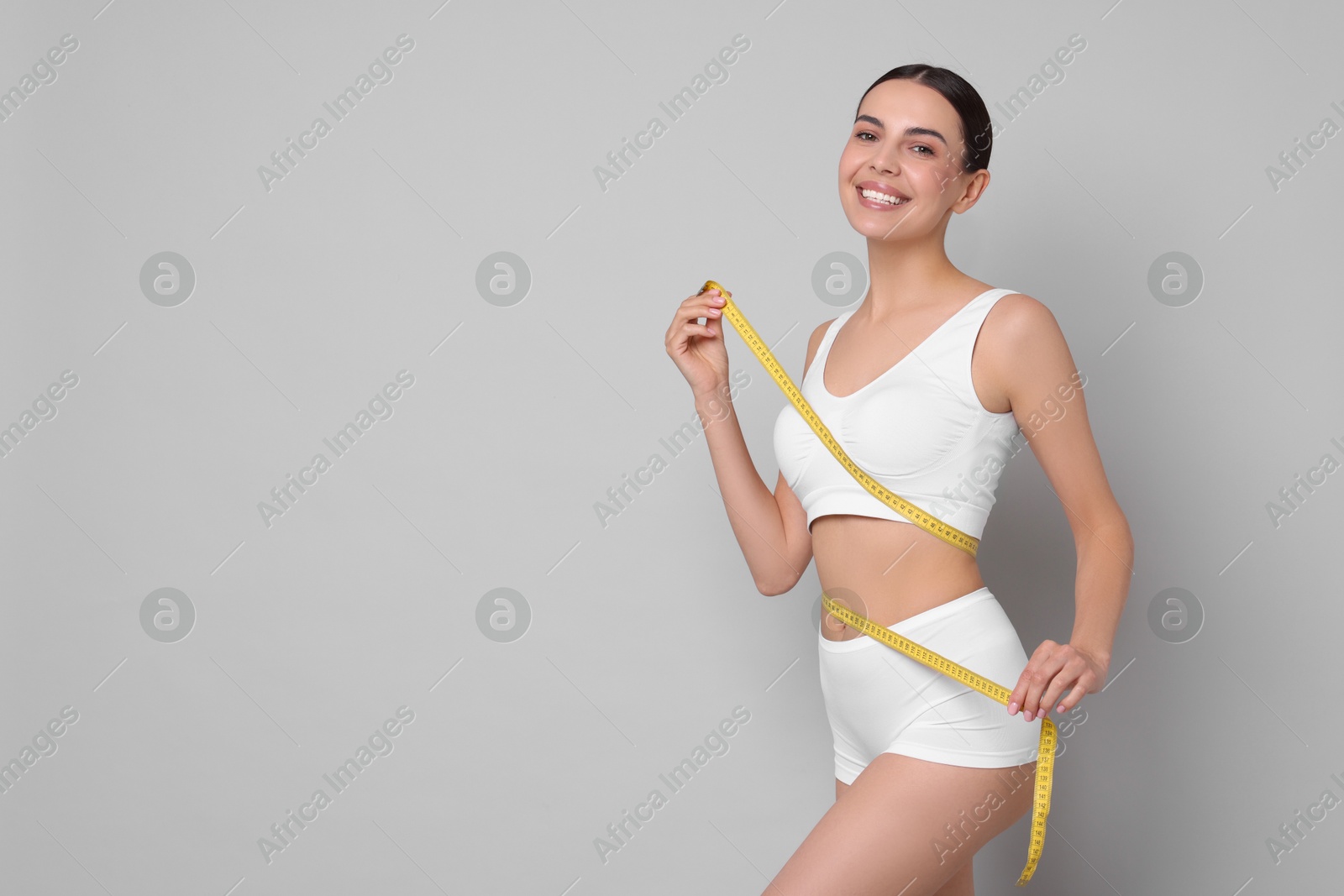 Photo of Diet and weight loss concept. Beautiful young woman with measuring tape showing her slim body against light grey background. Space for text