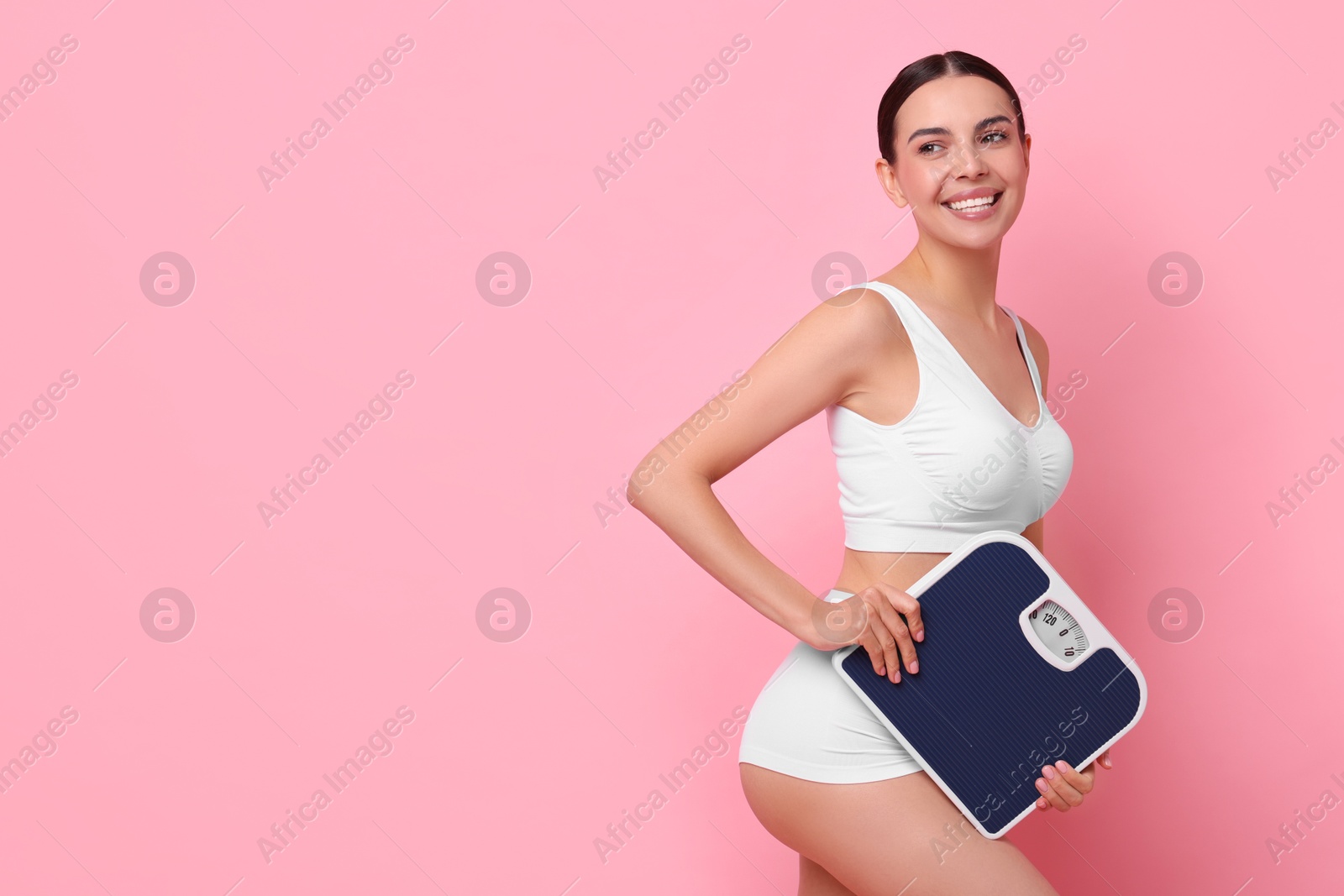 Photo of Diet and weight loss concept. Happy young woman with floor scale on pink background. Space for text