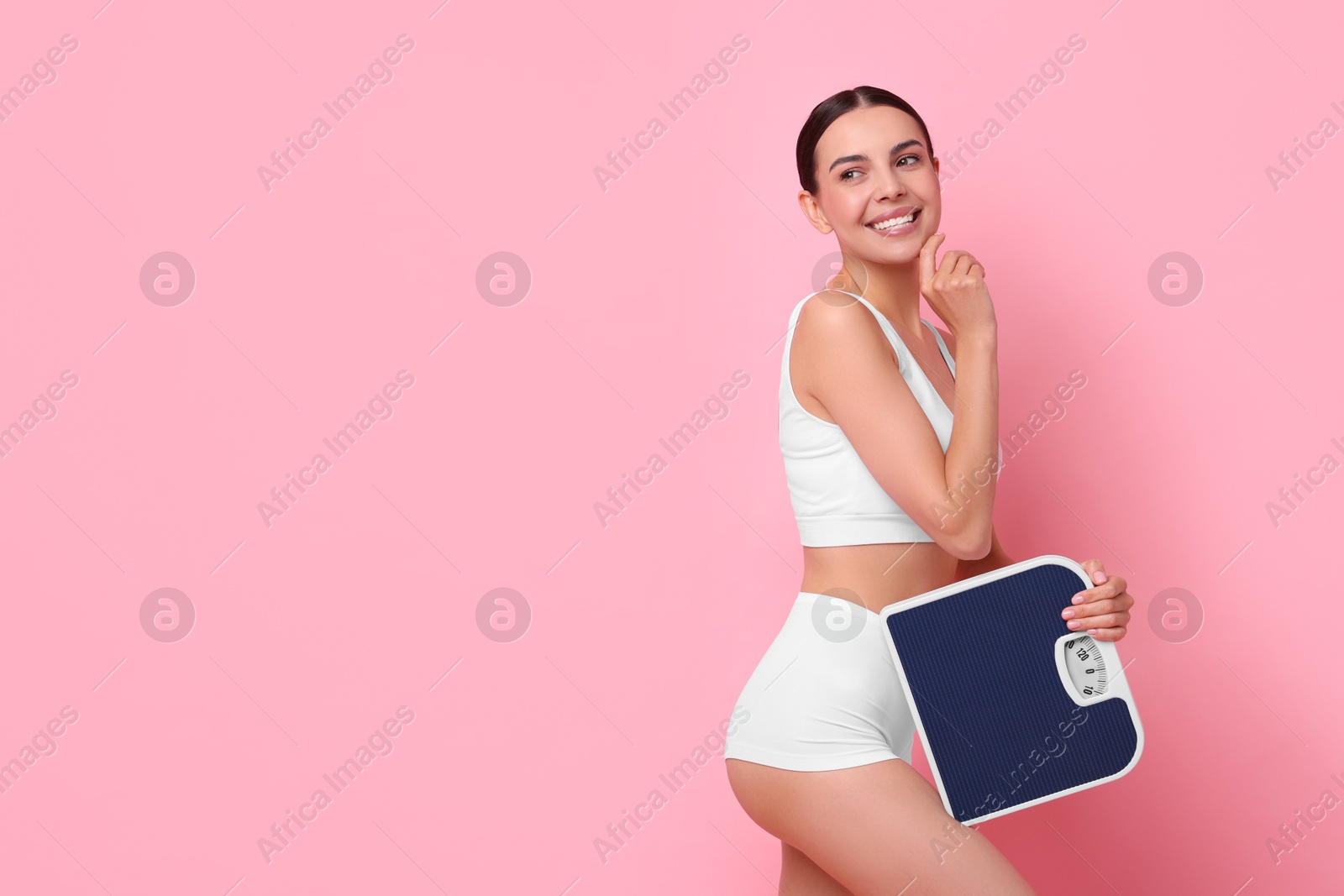 Photo of Diet and weight loss concept. Happy young woman with floor scale on pink background. Space for text