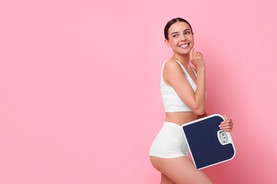 Photo of Diet and weight loss concept. Happy young woman with floor scale on pink background. Space for text