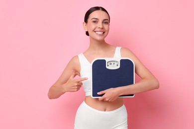 Diet and weight loss concept. Happy young woman with floor scale on pink background