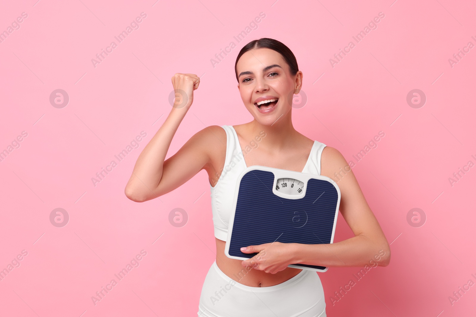 Photo of Diet and weight loss concept. Happy young woman with floor scale on pink background