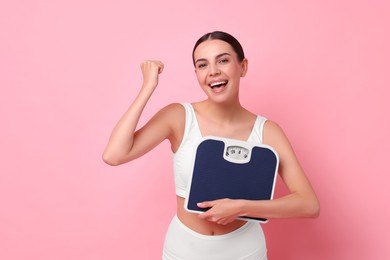 Photo of Diet and weight loss concept. Happy young woman with floor scale on pink background