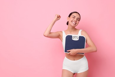 Photo of Diet and weight loss concept. Happy young woman with floor scale on pink background. Space for text