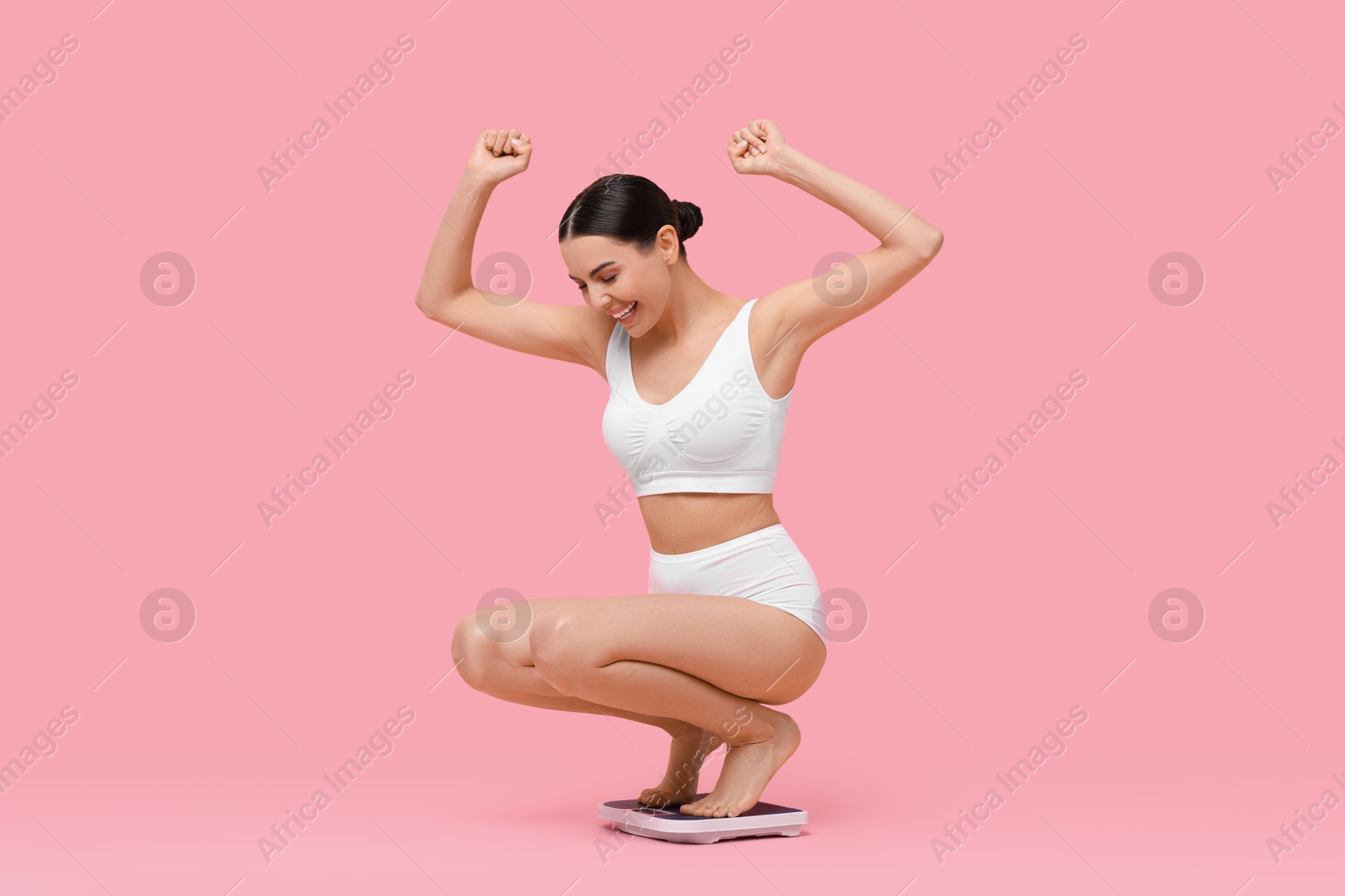 Photo of Diet and weight loss concept. Happy young woman on floor scale against pink background