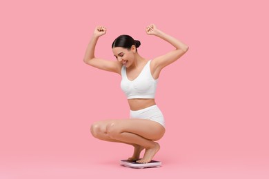 Diet and weight loss concept. Happy young woman on floor scale against pink background