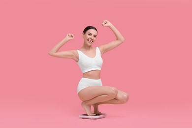 Photo of Diet and weight loss concept. Happy young woman on floor scale against pink background