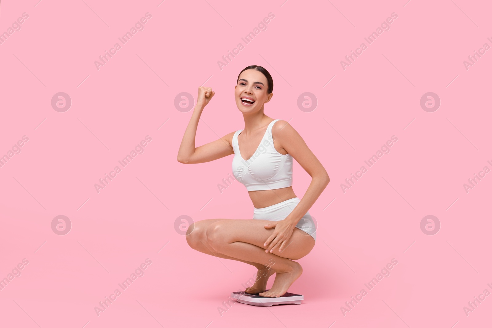 Photo of Diet and weight loss concept. Happy young woman on floor scale against pink background