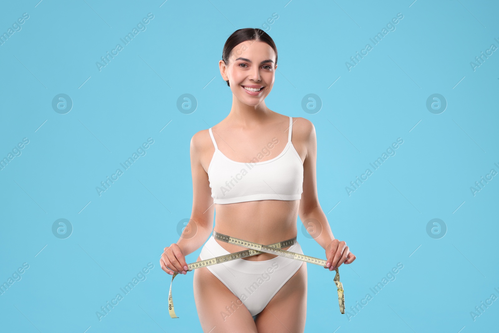 Photo of Diet and weight loss concept. Beautiful young woman with measuring tape showing her slim body against light blue background