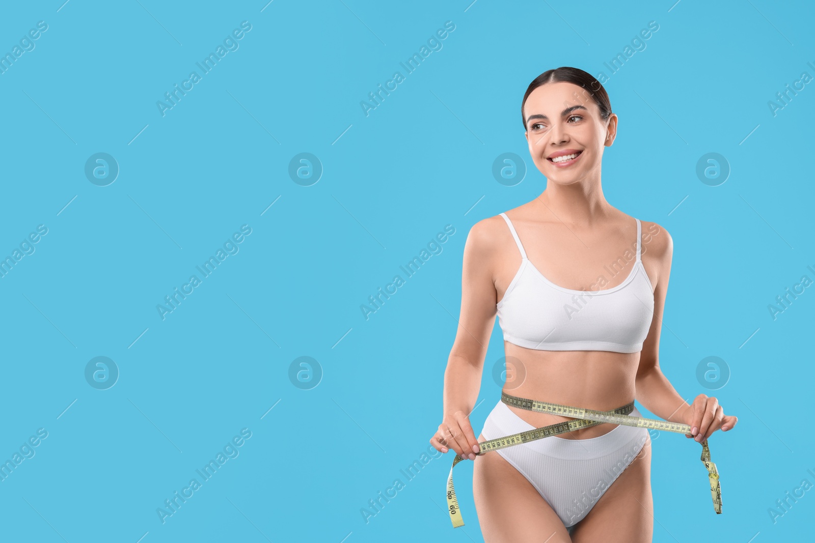 Photo of Diet and weight loss concept. Beautiful young woman with measuring tape showing her slim body against light blue background. Space for text