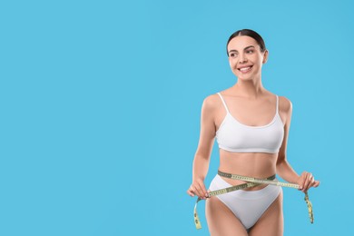 Diet and weight loss concept. Beautiful young woman with measuring tape showing her slim body against light blue background. Space for text