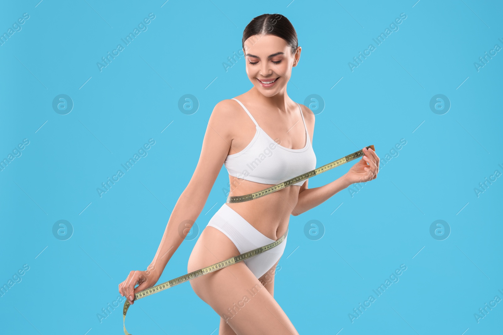 Photo of Diet and weight loss concept. Beautiful young woman with measuring tape showing her slim body against light blue background