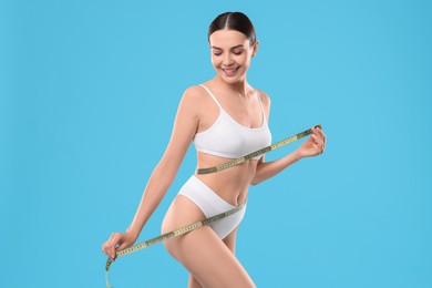 Photo of Diet and weight loss concept. Beautiful young woman with measuring tape showing her slim body against light blue background