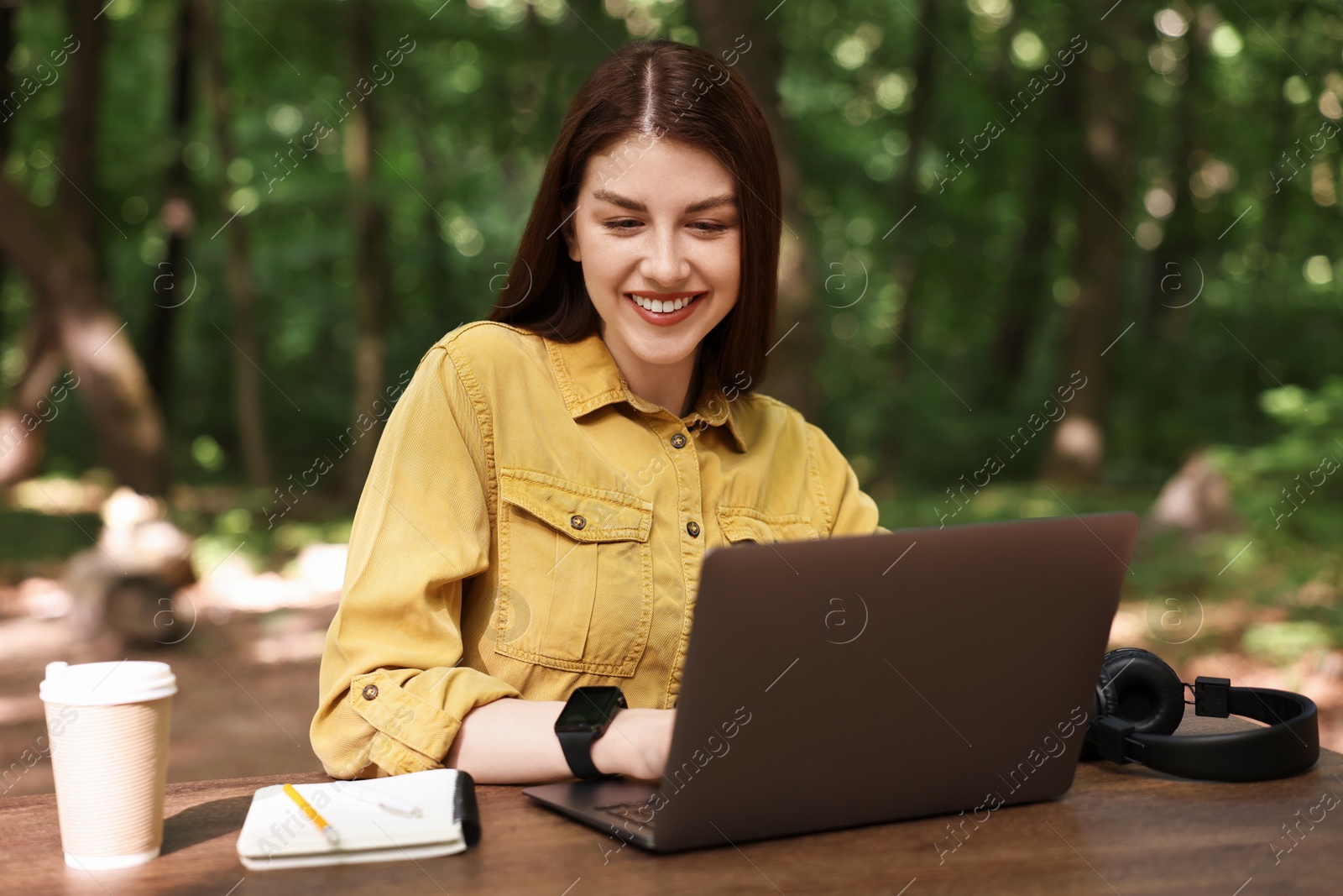 Photo of Smiling freelancer working with laptop at table outdoors. Remote job