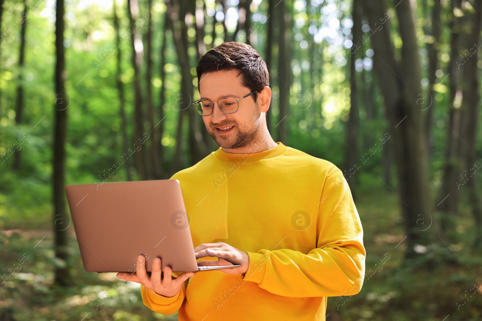 Photo of Smiling traveler working with laptop outdoors on sunny day. Remote job