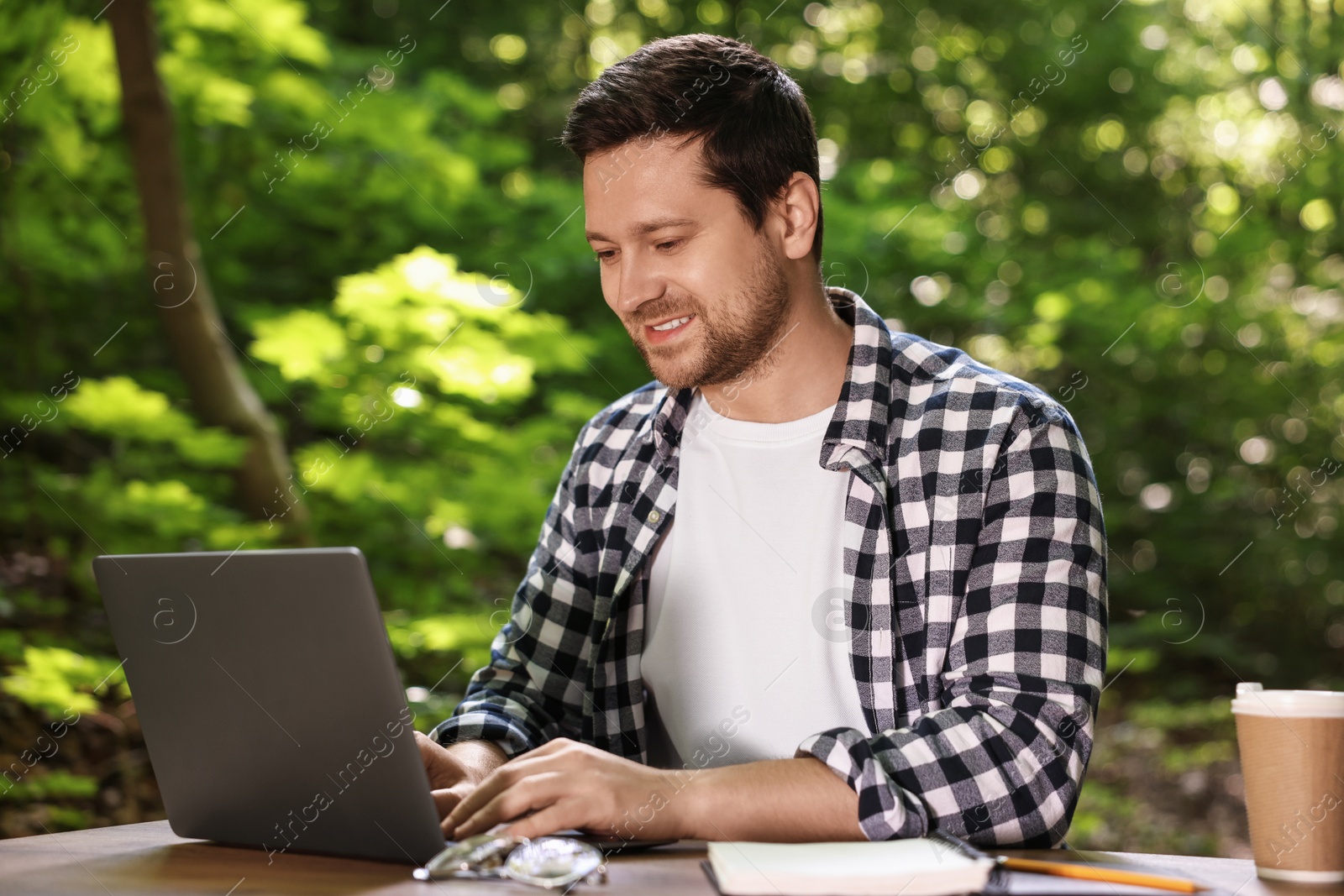 Photo of Smiling freelancer working with laptop at table outdoors. Remote job