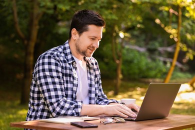 Smiling freelancer working with laptop at table outdoors. Remote job