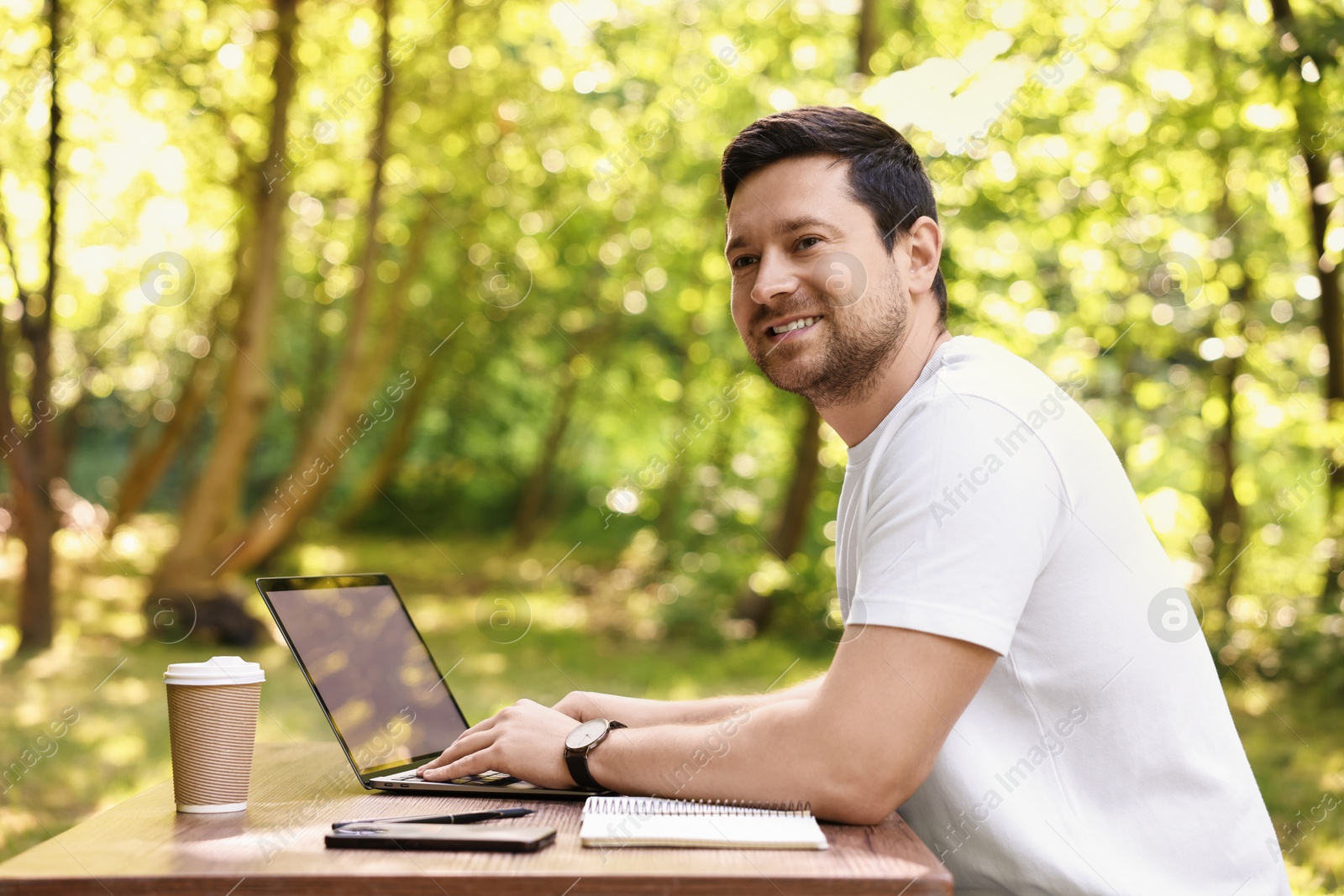 Photo of Smiling freelancer working with laptop at table outdoors. Remote job