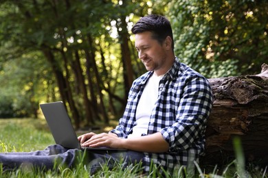 Smiling freelancer working with laptop on green grass in forest. Remote job