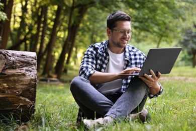 Photo of Smiling freelancer working with laptop on green grass in forest. Remote job
