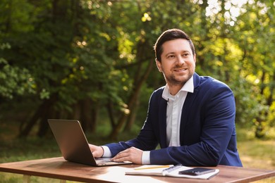 Photo of Smiling businessman working with laptop at table outdoors. Remote job