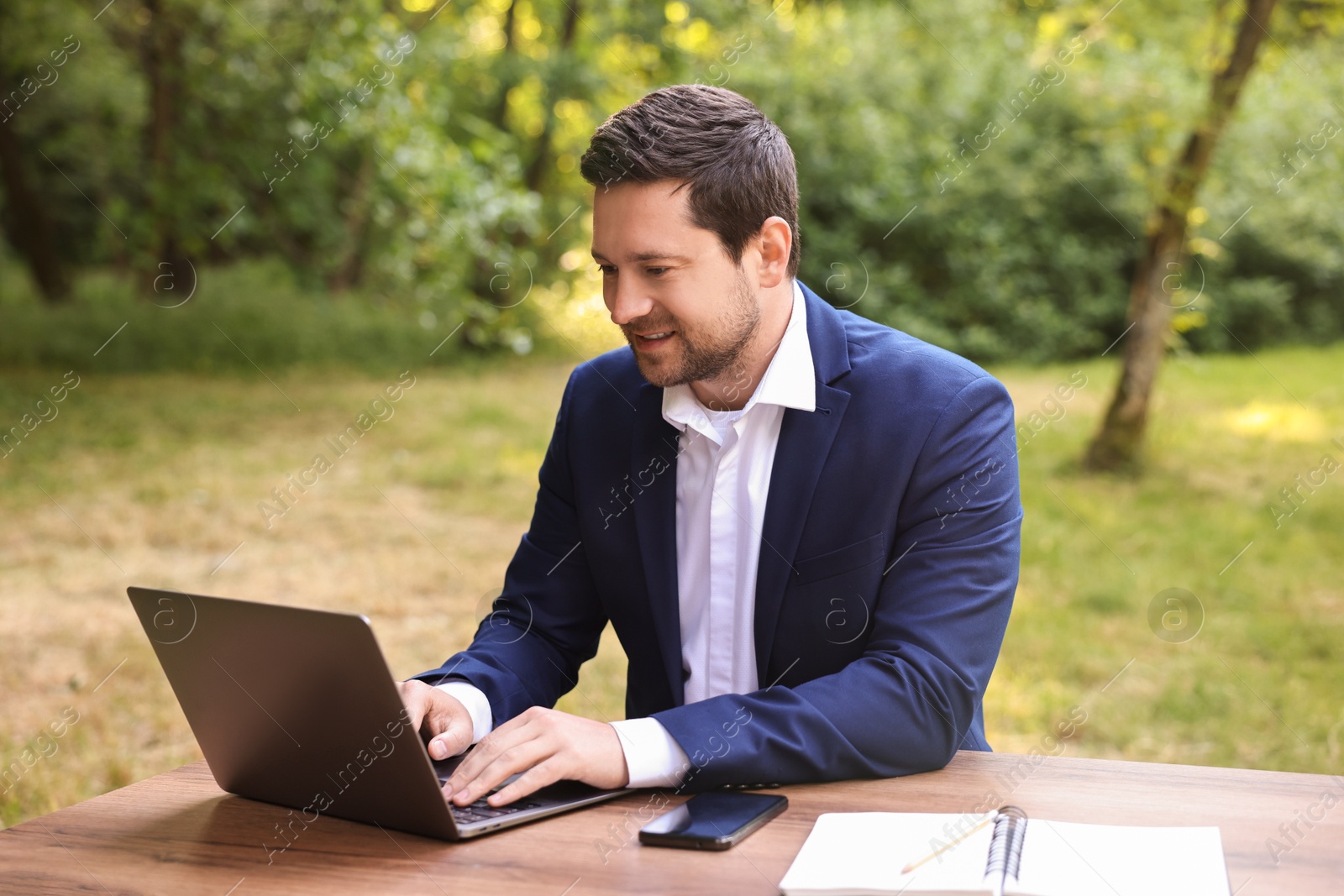 Photo of Smiling businessman working with laptop at table outdoors. Remote job