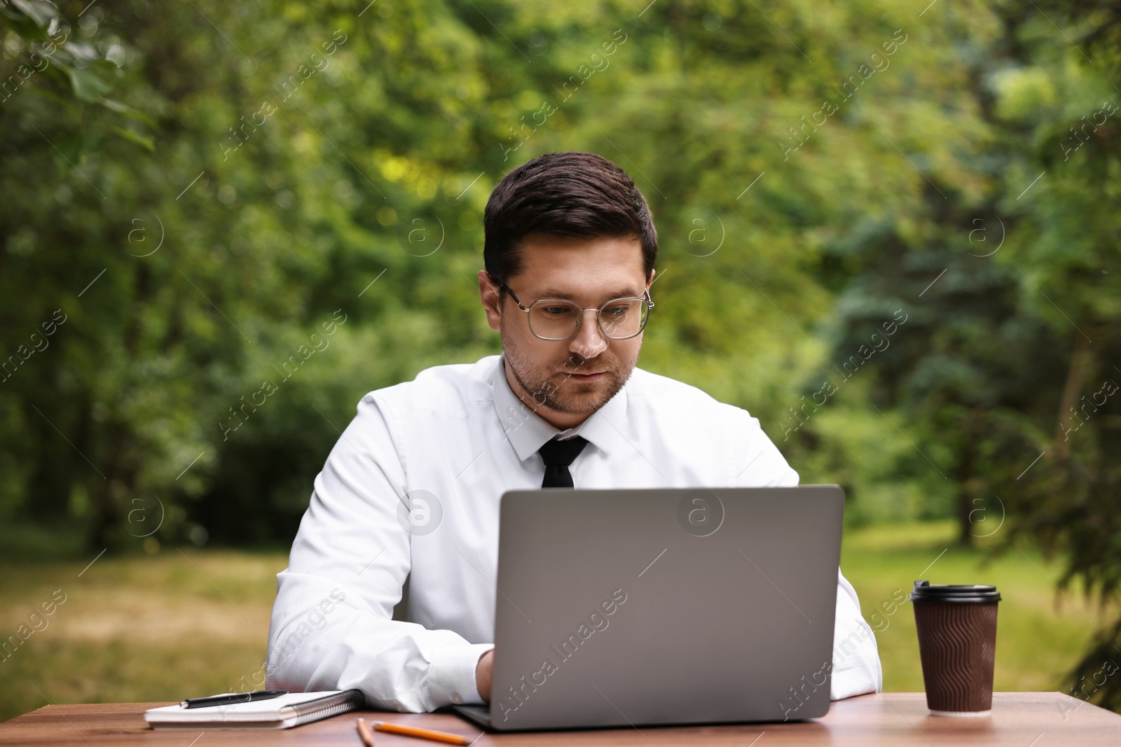 Photo of Businessman working with laptop at table outdoors. Remote job