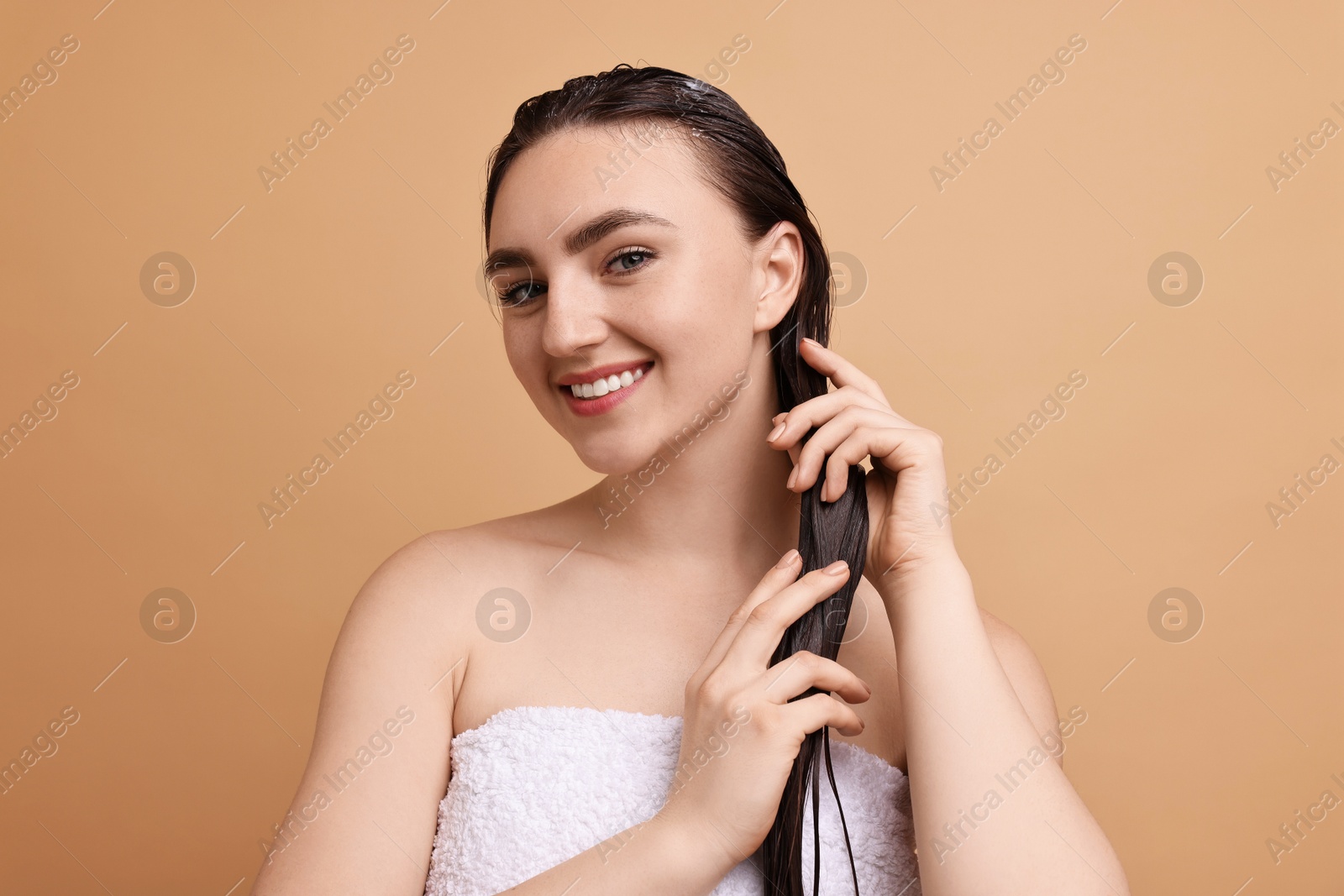 Photo of Smiling woman applying hair mask on beige background