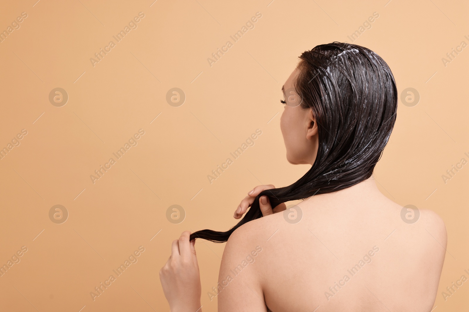 Photo of Woman applying hair mask on beige background, back view. Space for text