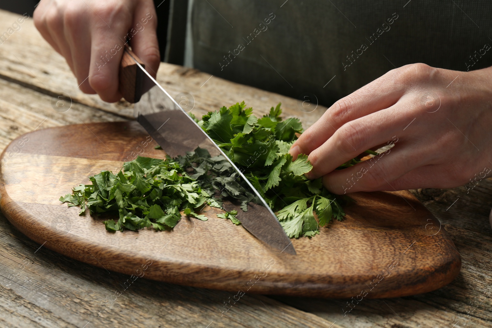 Photo of Woman cutting fresh coriander at wooden table, closeup