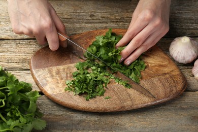 Photo of Woman cutting fresh coriander at wooden table, closeup