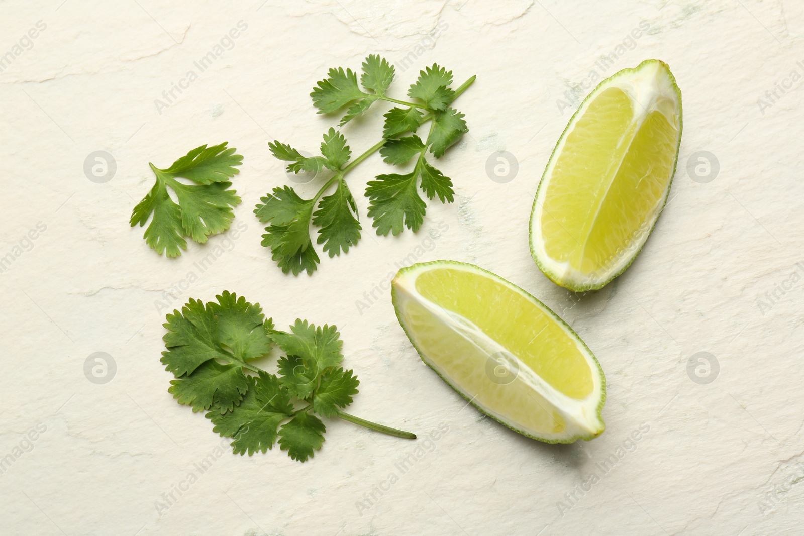 Photo of Fresh coriander leaves and lime wedges on light textured table, flat lay