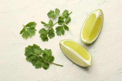 Fresh coriander leaves and lime wedges on light textured table, flat lay