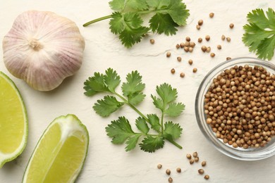 Fresh coriander leaves, dried seeds, garlic and lime wedges on light textured table, flat lay