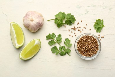 Fresh coriander leaves, dried seeds, garlic and lime wedges on light textured table, flat lay