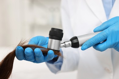 Trichologist with dermatoscope examining patient`s hair in clinic, closeup