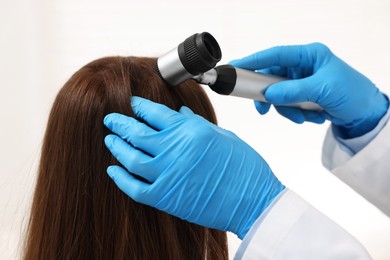 Photo of Trichologist with dermatoscope examining patient`s hair in clinic, closeup