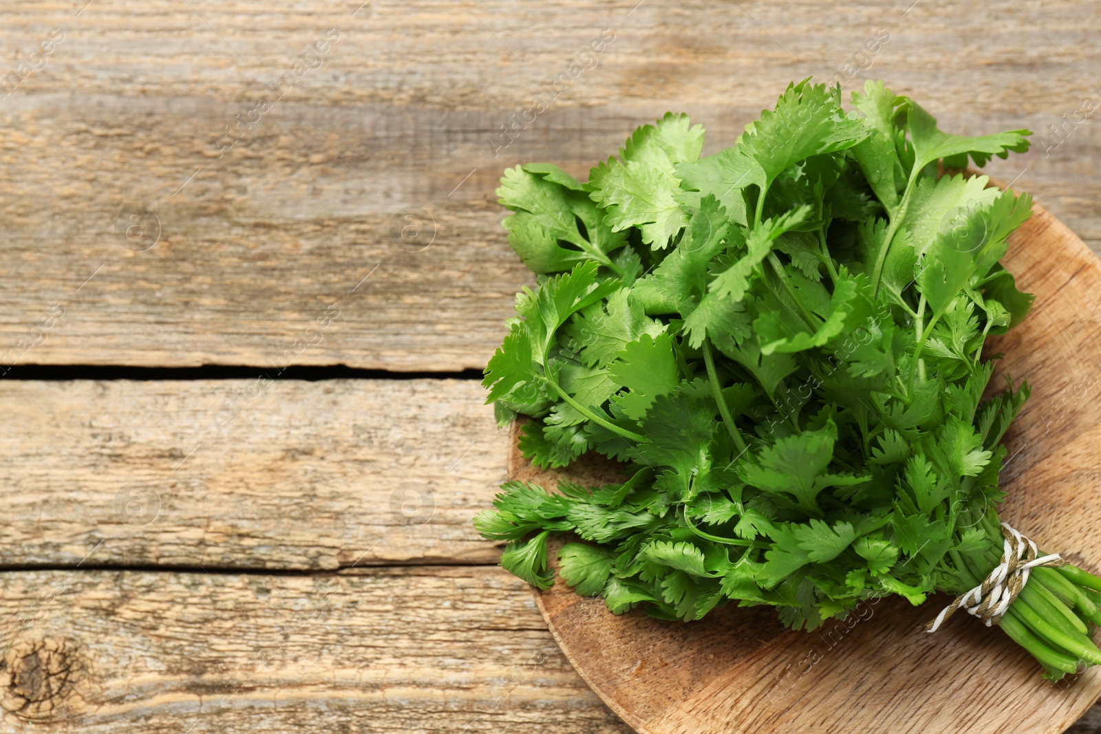 Photo of Bunch of fresh coriander on wooden table, top view. Space for text